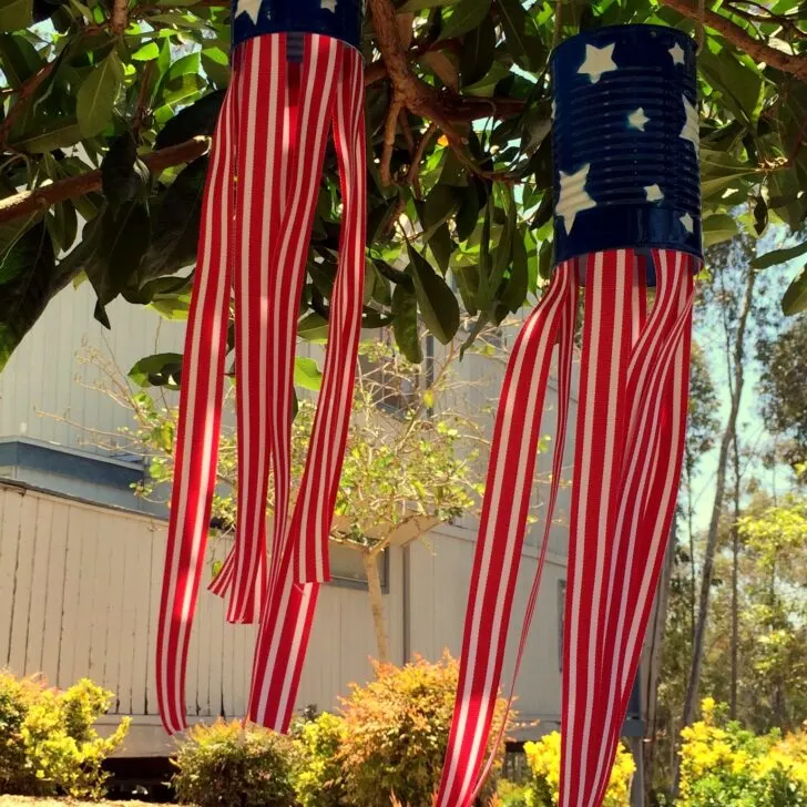 Using cans, spray paint, and ribbon, make these super cute windsocks to add a little red, white, and blue to your yard #4thofJuly #upcycled #craftproject
